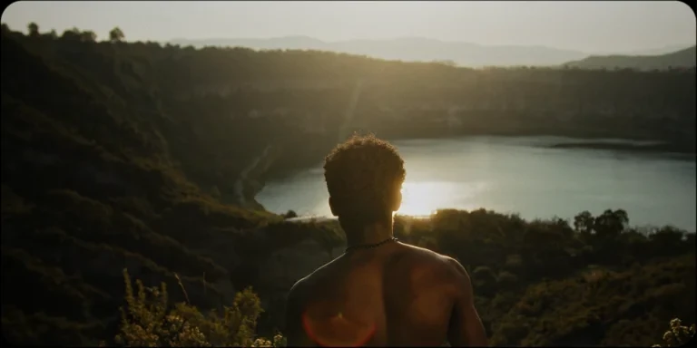 Fotograma: figura frente a un lago al atardecer